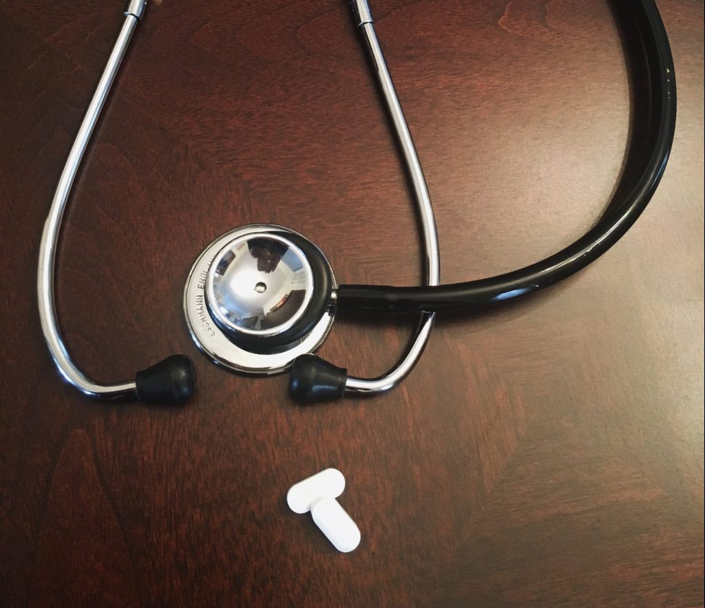 This image shows a Stethoscope and two pills kept on a brown table